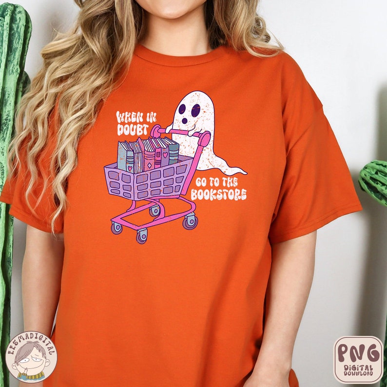 K&ouml;nnte beinhalten: Orangefarbenes T-Shirt mit einem Geist, der einen Einkaufswagen voller B&uuml;cher schiebt. Der Text auf dem Shirt lautet "When in doubt, go to the bookstore".