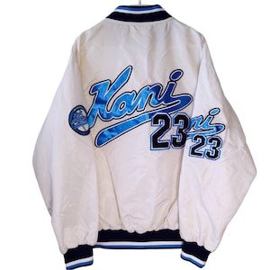 May include: White satin jacket with blue and black accents. Features the word "Kani" in large, stylized blue lettering on the back, along with the number "23". The jacket has a navy blue collar, cuffs, and waistband with white stripes.