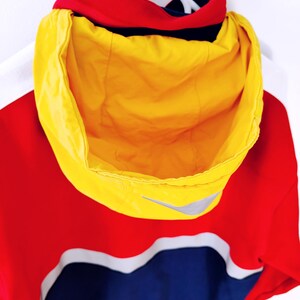 May include: A hooded jacket in red, yellow, and blue, with a white accent stripe. The hood is bright yellow, and the jacket features a small silver logo. The jacket is hanging on a white hanger.