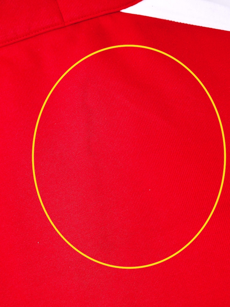 May include: Close-up of a vibrant red fabric with a subtle texture. The fabric appears to be part of a garment, with a white collar visible at the top. The material has a smooth, slightly shiny appearance.