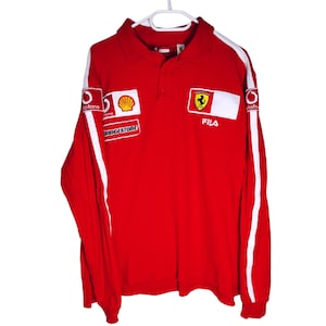 Könnte beinhalten: Rotes Langarm-Polo-Shirt mit weißen Akzenten und Kragen. Mit Sponsorenlogos und einem Ferrari-Emblem. Das Shirt ist von Fila.