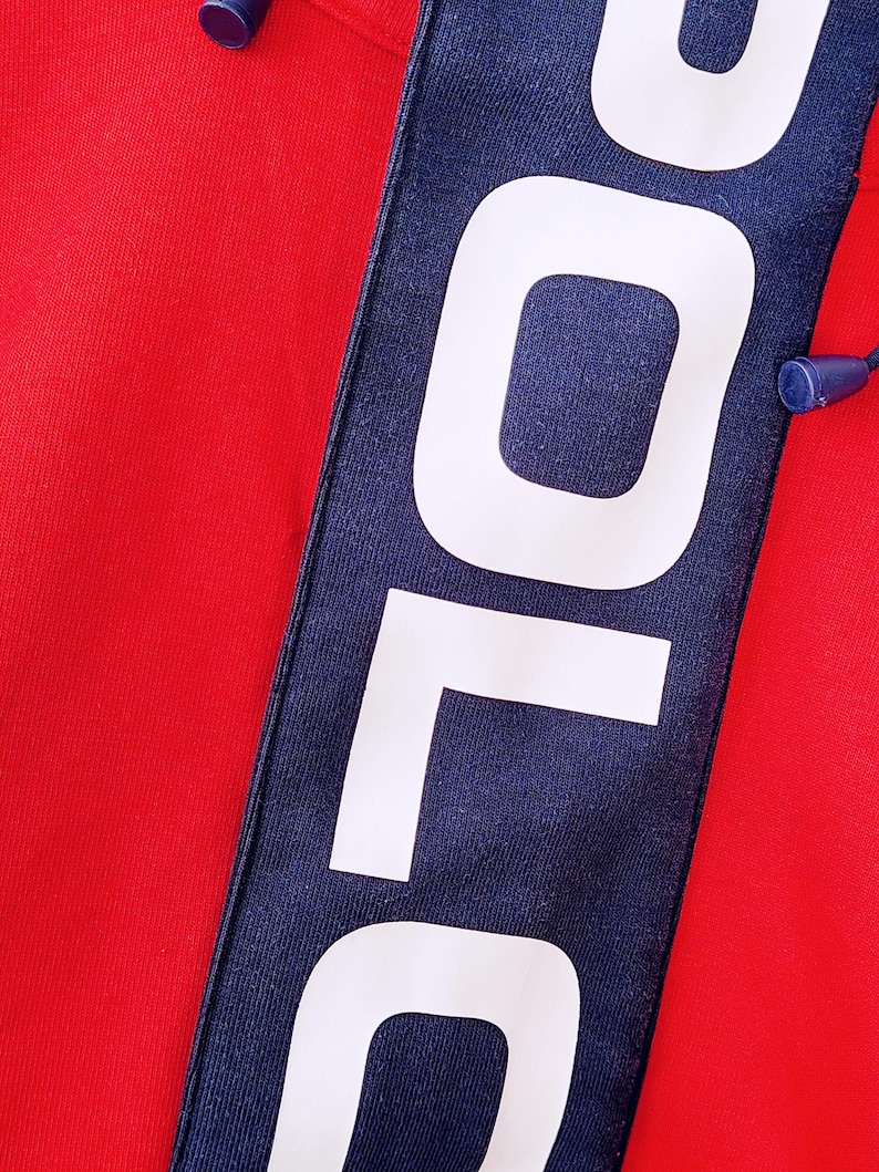 May include: Close-up of a red garment with a navy blue stripe. The stripe features the word "POLO" in large white capital letters. A blue drawstring is visible at the top. The fabric appears to be a knit material.