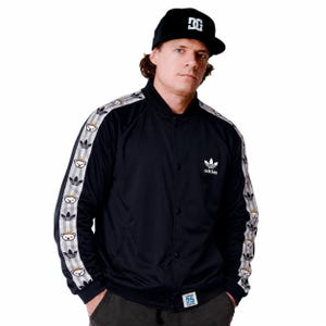 Op de afbeelding: Een zwart Adidas bomberjack met een wit Adidas-logo op de borst en een klein wit label aan de zoom. De mouwen hebben grijze en witte verticale strepen versierd met een herhalend patroon van berengezichten en zwarte klaverbladlogo's.