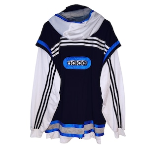 Op de afbeelding: Een vintage Adidas-jack in marineblauw, wit en blauw. De jas heeft het Adidas-logo in een blauwe ovaal op de rug, witte strepen op de mouwen en een capuchon. Retro sportief ontwerp.