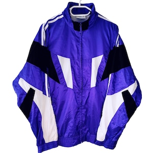 May include: A vintage purple, black, and white track jacket with a full zipper closure. The jacket features a high collar and elastic cuffs and hem. The design includes white and black geometric shapes across the front and sleeves. The jacket is hanging on a white hanger.