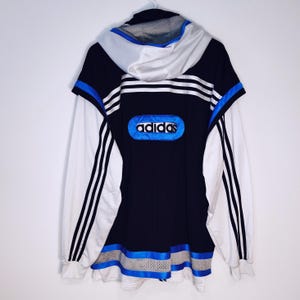 May include: Black and white Adidas jacket with blue accents. The jacket features the Adidas logo in a blue oval on the back, three stripes down the sleeves, and a hood. The jacket has a sporty design.