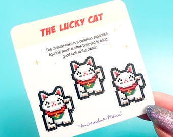 Op de afbeelding: Drie pixel art gelukkat stickers op een witte kaart met de tekst "THE LUCKY CAT" en "The maneki-neko is a common Japanese figurine which is often believed to bring good luck to the owner." en "Lavendar Floss".