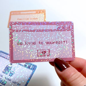 Peut inclure: Un autocollant holographique rose et bleu avec un design de fen&ecirc;tre d'ordinateur. La fen&ecirc;tre indique "REMINDER" dans la barre de titre et "Be Kind to Yourself!" dans le corps de la fen&ecirc;tre.