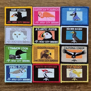 May include: A collection of embroidered patches featuring various bird species, each with a unique illustration and name. The patches are rectangular with a colored border and include the text "Holy City Birding".