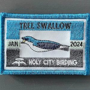 May include: A blue and white embroidered patch with the text "TREE SWALLOW" and "HOLY CITY BIRDING". The patch also includes the text "JAN 2024" and an image of a tree swallow.