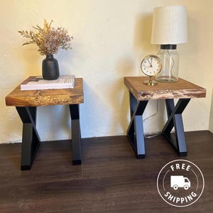 May include: Two wooden end tables with black X-shaped legs. The table on the right has a small gold clock on top.
