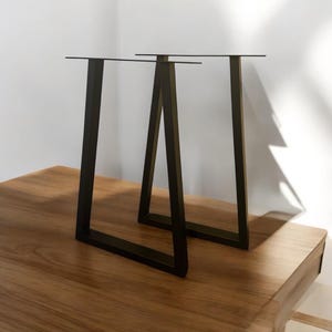 May include: Two black metal table legs in an A-frame design. The legs are made of sturdy metal and have a black powder-coated finish.