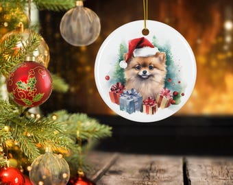 Puede incluir: Adorno navideño redondo con un perro Pomerania con un gorro de Papá Noel, rodeado de regalos envueltos y árboles de hoja perenne. El adorno cuelga de una cuerda dorada, con un árbol de Navidad y otros adornos en el fondo.