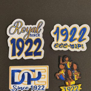 May include: Four embroidered patches with white, blue, and gold designs. The patches feature the text "Royal Since 1922", "1922", "DPE Since 1922", and a graphic with the year 1922. The patches are likely for apparel.
