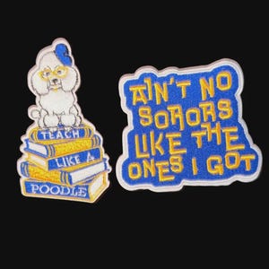 May include: Two embroidered patches. One features a white poodle wearing glasses and a blue bow, sitting atop a stack of books with the text "Teach Like a Poodle." The other patch reads "Ain't No Sorors Like The Ones I Got."