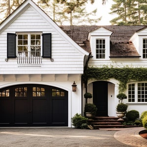 May include: A two-story white house with a black garage door and shutters. The house has a brown shingled roof and is surrounded by lush greenery, including bushes and trees. A brick pathway leads to the front door.