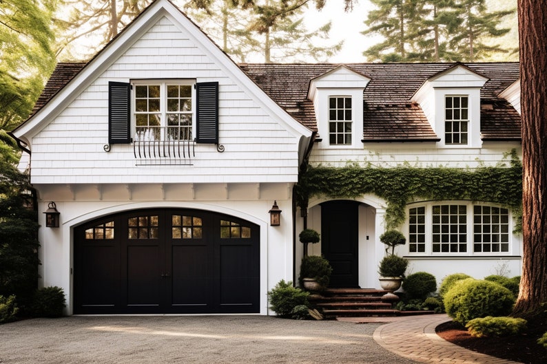 May include: A two-story white house with a black garage door and shutters. The house has a brown shingled roof and is surrounded by lush greenery, including bushes and trees. A brick pathway leads to the front door.