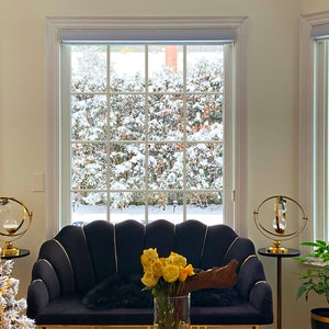 May include: A living room scene with a black velvet sofa, gold accents, and a Christmas tree. A large window offers a view of a snowy landscape. Yellow roses in a vase add a pop of color.