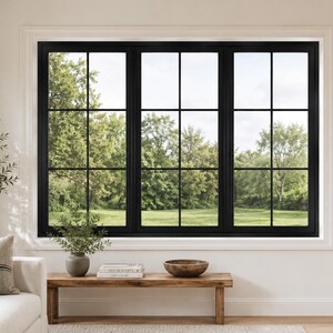 May include: A large, black-framed window with a grid pattern, offering a view of a lush green landscape. The window is set in a white wall, with a wooden bench and decorative items in front.