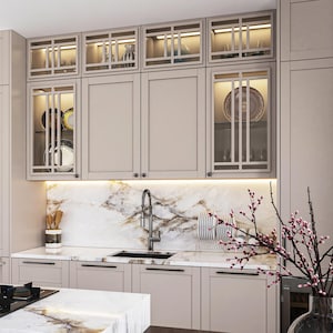 May include: A contemporary kitchen featuring light beige cabinetry and a marble worktop. Glass-fronted upper cabinets display crockery. A stainless steel sink and tap are centrally positioned. A vase of pink flowers adorns the counter.