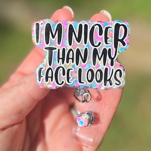 May include: A sparkly pink, blue, and white badge holder with the text "I'm nicer than my face looks".