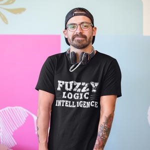 Könnte beinhalten: Ein schwarzes T-Shirt mit einem weißen Aufdruck, der "Fuzzy Logic Intelligence" lautet. Die Person, die das Shirt trägt, hat einen Bart und trägt eine schwarze Baseballkappe.