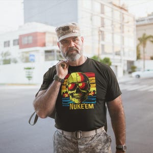 May include: A black t-shirt with a retro-style skull graphic wearing sunglasses and the text "NUKE'EM" underneath. The skull is surrounded by a rainbow-colored stripe.