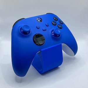 May include: A bright blue Xbox controller with a black faceplate and buttons. The controller is on a blue stand.