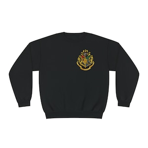 May include: Black sweatshirt with a gold embroidered Hogwarts crest on the front. The crest features a shield with the Hogwarts house colours and the Hogwarts motto "Draco Dormiens Nunquam Titillandus".