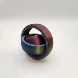May include: A metallic ring with a rainbow iridescent finish. The ring is made of two interlocking circles, creating a unique and modern design.