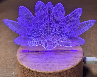 以下が含まれることがあります： 木製の台座に置かれた、紫色の3Dプリントされた蓮の花のナイトライト。ライトはUSBケーブルで接続されています。
