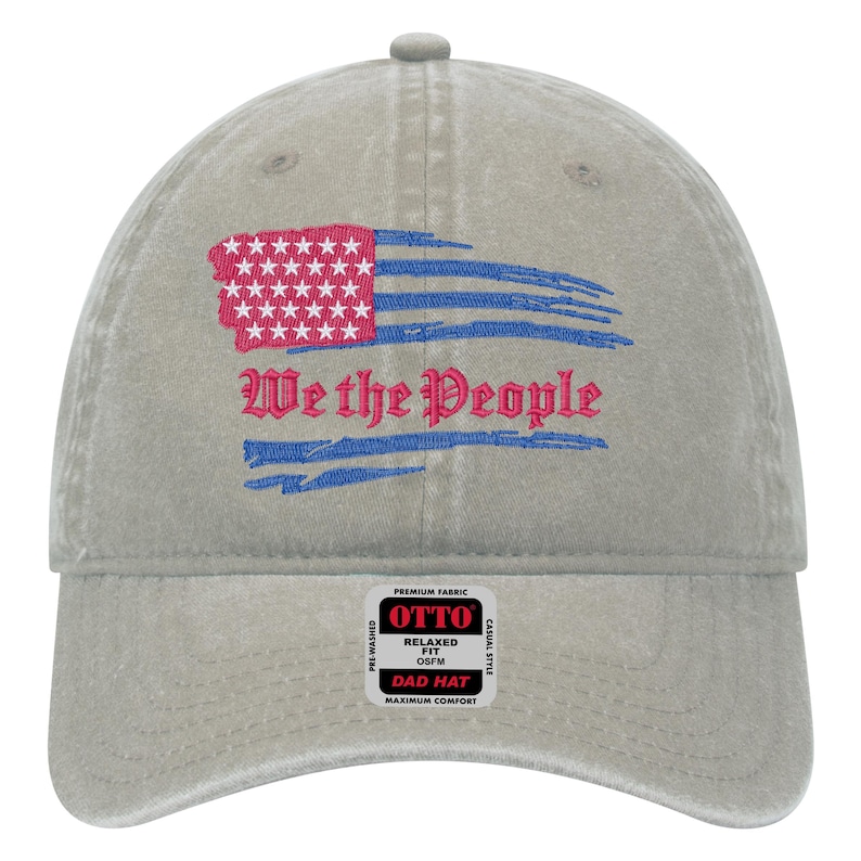 May include: A gray cotton baseball cap with a distressed American flag and the text "We the People" embroidered on the front. The cap has a relaxed fit and is labeled "Otto Dad Hat".