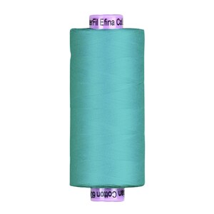 May include: A spool of teal-colored thread, labeled "Efina Cotton 60." The thread is tightly wound around a cylindrical core. The spool's top and bottom are a light purple color, with the brand name printed on the top.