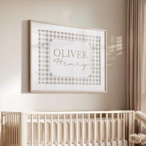 May include: A neutral-toned nursery with a wooden cot, a framed print reading "Oliver Henry", and a teddy bear. The print has a gingham pattern. A round rug and a woven basket complete the decor.