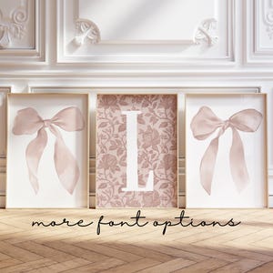 May include: Three framed prints. Two feature a watercolor bow in blush pink. The center print has a floral pattern background with a white letter "L". The text "more font options" is written in cursive at the bottom.