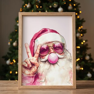 May include: A watercolor illustration of Santa Claus wearing pink sunglasses and blowing a pink bubble. He is giving the peace sign with his left hand. The background is a light pink color.