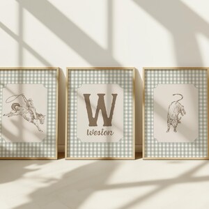 May include: Three framed prints with a Western theme. The prints feature a cowboy on a bucking bronco, a large letter "W" with the name "Weston" below, and a bull. The frames have a gold finish and a light green and white checkered border.