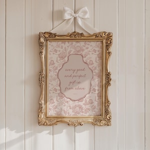Puede incluir: Una impresión enmarcada con el texto "every good and perfect gift is from above". La impresión tiene un patrón floral en tonos rosas y está enmarcada en un marco dorado ornamentado. Una cinta y un lazo blancos están unidos en la parte superior.