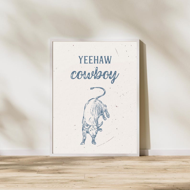 K&ouml;nnte beinhalten: Ein wei&szlig;er gerahmter Druck mit einer blauen Bullenillustration und dem Text "Yeehaw cowboy" in Blau.