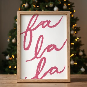 May include: A framed print with the words "fa la la" written in a pink cursive font on a white background.