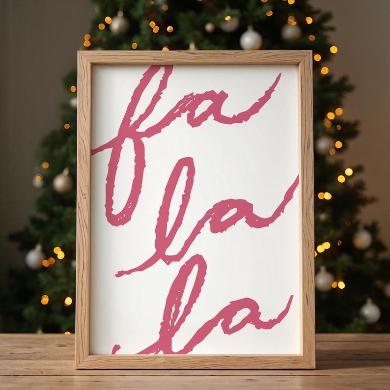 May include: A framed print with the words "fa la la" written in a pink cursive font on a white background.