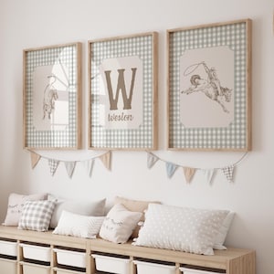 May include: Three framed prints with a Western theme. One print features a bucking bronco, another a letter "W" with the name "Weston", and the third a drawing of a bull. The frames are light wood, and the background is a gingham pattern.