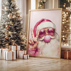 May include: A pink and white Santa Claus wearing sunglasses and blowing a bubble with a peace sign. The background is a light pink color.