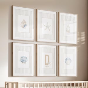 May include: A set of six framed wall art prints featuring watercolor illustrations of seashells and a starfish. One print displays the letter D and the name Dylan. Each print has a light beige striped border and is housed in a light wood frame.