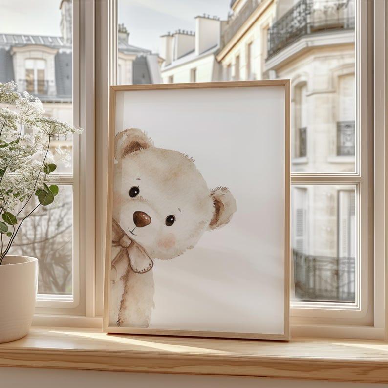 Puede incluir: Una impresi&oacute;n enmarcada con una ilustraci&oacute;n de acuarela de un oso de peluche asom&aacute;ndose. El oso tiene pelaje marr&oacute;n claro, una nariz marr&oacute;n y un peque&ntilde;o lazo. El marco es de madera clara.