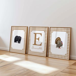 May include: Three framed prints with a brown and white gingham pattern border. The left print features a black bear, the middle print features the letter E with the name Emmett below, and the right print features a brown and gray turkey.