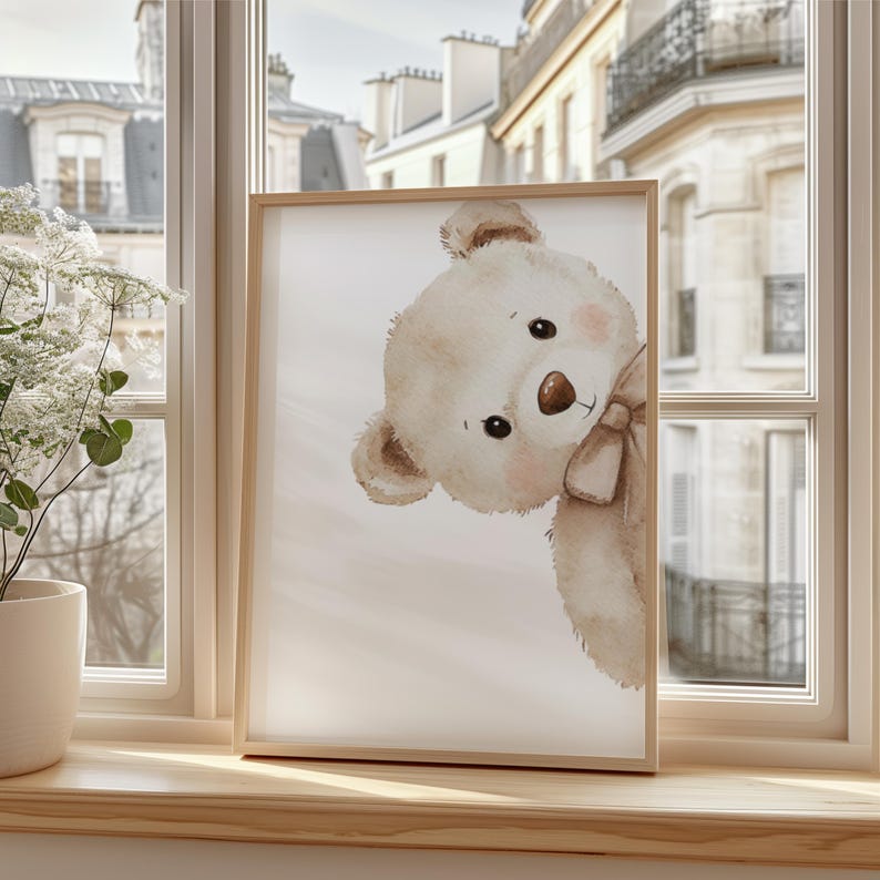 Puede incluir: Impresi&oacute;n enmarcada con una ilustraci&oacute;n de acuarela de un oso de peluche mirando de reojo. El oso es de color marr&oacute;n claro con un lazo a juego y mejillas rosadas. El marco es de madera clara y la impresi&oacute;n est&aacute; en un alf&eacute;izar.