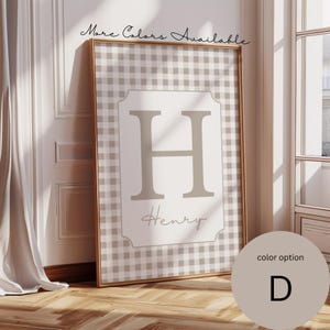 May include: Framed wall art featuring a tan and white gingham pattern. The artwork displays a large letter "H" and the name "Henry" in a soft, neutral color. The frame is gold, and the text "More Colors Available" is written at the top.
