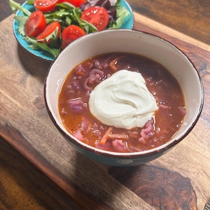 Peut inclure: Un bol de soupe rouge garni d'une cuillerée de crème blanche, servi avec une salade de tomates et de verdure. La soupe est dans un bol turquoise, et la salade dans un bol similaire. Le tout est présenté sur une planche en bois.