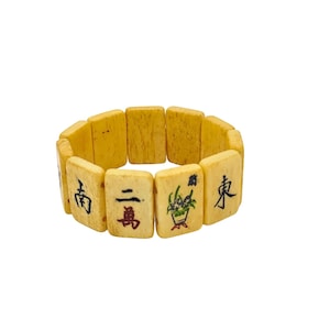 Könnte beinhalten: Ein Vintage-Armband aus rechteckigen, cremefarbenen Kacheln. Jede Kachel zeigt schwarze und rote chinesische Schriftzeichen und farbenfrohe Illustrationen. Das Armband ist dehnbar und passt sich dem Handgelenk an.